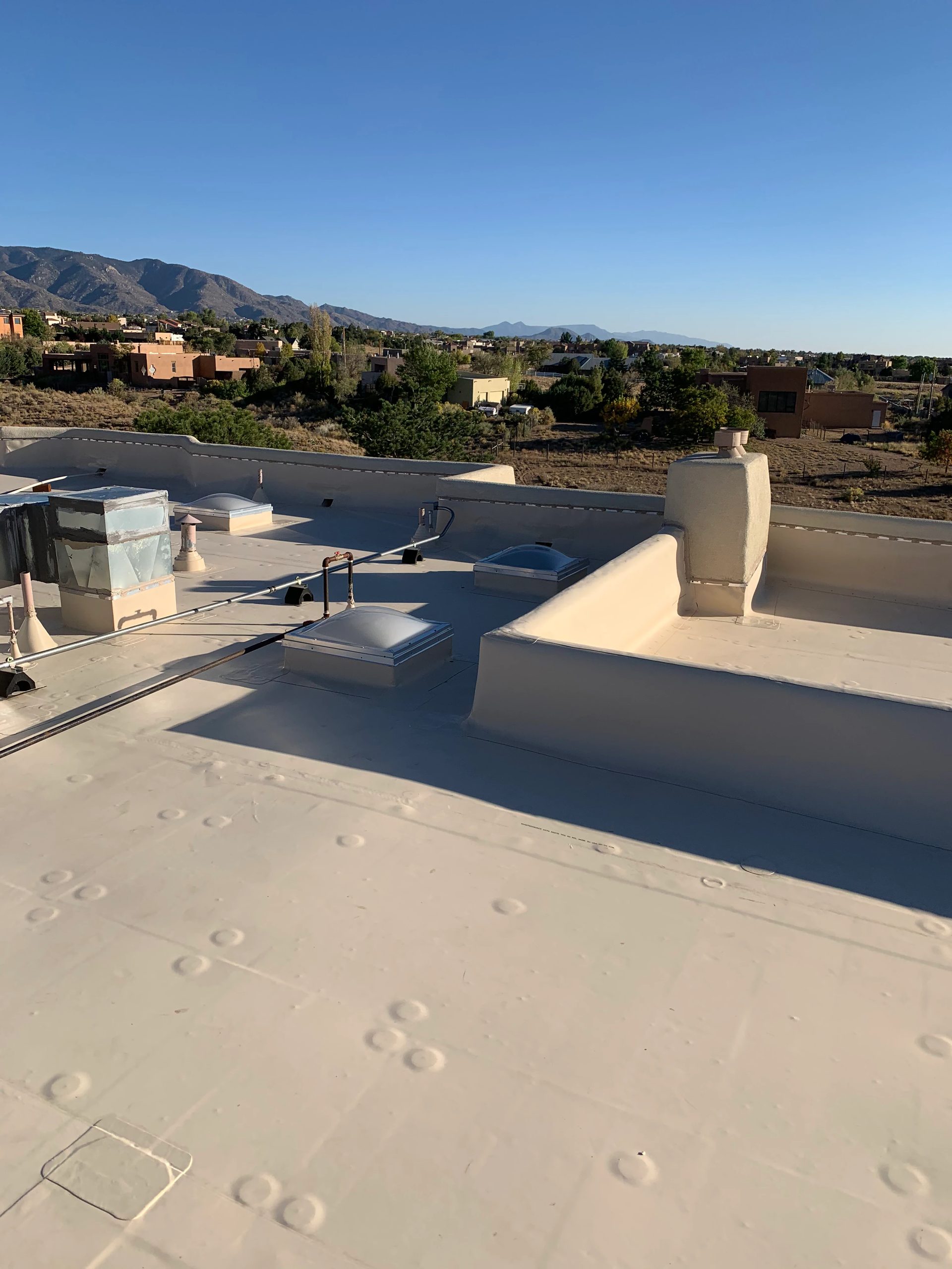 Flat foam roof with a parapet and a clear mountain range behind the New Mexico high desert